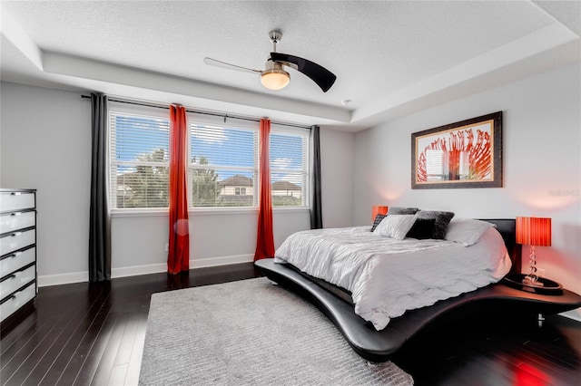 bedroom with ceiling fan, dark hardwood / wood-style floors, a textured ceiling, and a raised ceiling