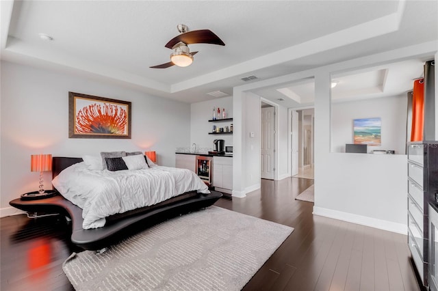 bedroom with a tray ceiling, ceiling fan, and dark wood-type flooring