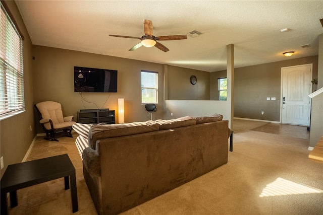 living area with baseboards, visible vents, a ceiling fan, and light colored carpet