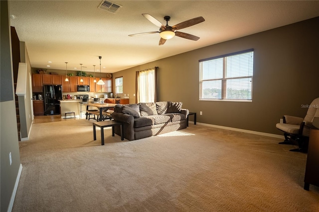 living area with light carpet, baseboards, visible vents, a ceiling fan, and a textured ceiling