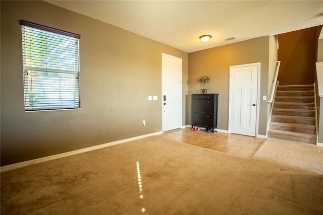 interior space with light carpet, baseboards, visible vents, stairway, and a textured ceiling