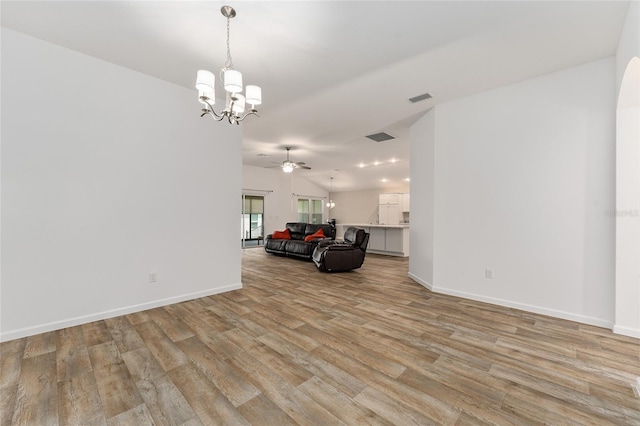 unfurnished living room featuring ceiling fan with notable chandelier, light hardwood / wood-style floors, and vaulted ceiling