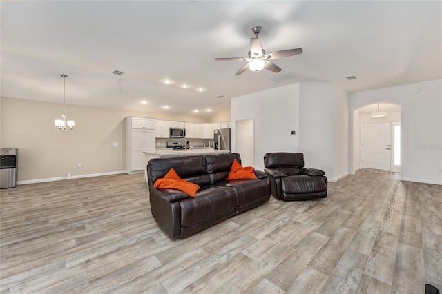 living room with lofted ceiling, light hardwood / wood-style floors, and ceiling fan with notable chandelier