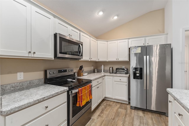 kitchen with white cabinetry, light wood-type flooring, light stone countertops, vaulted ceiling, and appliances with stainless steel finishes