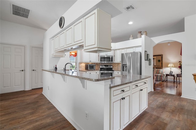 kitchen with appliances with stainless steel finishes, tasteful backsplash, sink, dark stone counters, and dark wood-type flooring