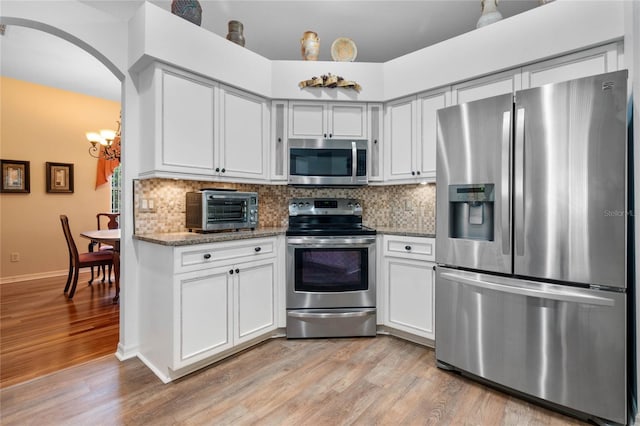 kitchen featuring appliances with stainless steel finishes, light hardwood / wood-style flooring, decorative backsplash, and light stone countertops