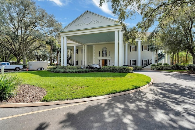 neoclassical / greek revival house with driveway, a front lawn, and stucco siding