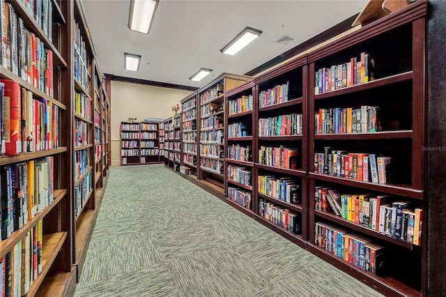 interior space featuring carpet, ornamental molding, wall of books, and visible vents