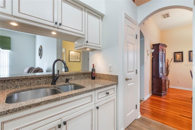 kitchen featuring visible vents, arched walkways, light stone countertops, light wood-type flooring, and a sink