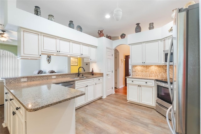 kitchen with arched walkways, stainless steel appliances, a sink, light wood-type flooring, and a peninsula