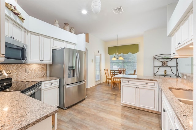 kitchen featuring light wood finished floors, stainless steel appliances, tasteful backsplash, a chandelier, and a peninsula