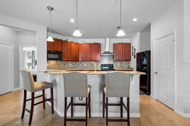 kitchen featuring light tile patterned floors, hanging light fixtures, black appliances, decorative backsplash, and wall chimney range hood