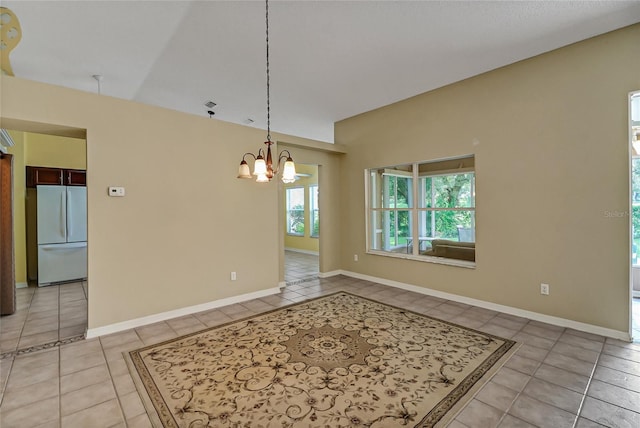 spare room featuring a chandelier, light tile patterned flooring, and baseboards