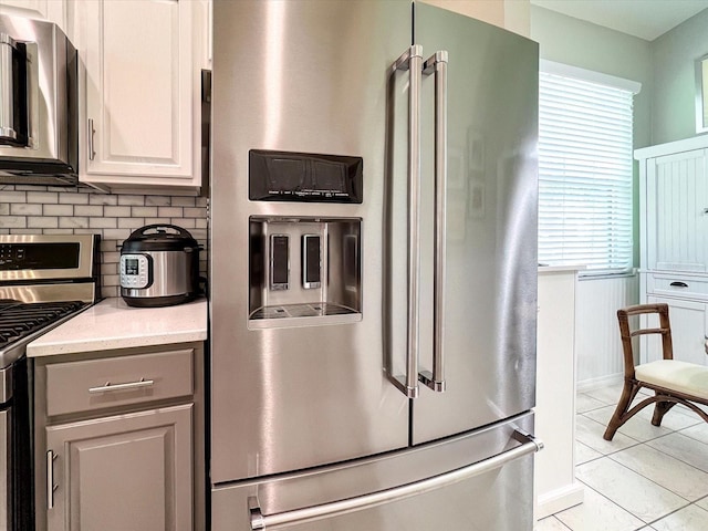 kitchen with stainless steel appliances, decorative backsplash, white cabinetry, light stone counters, and light tile patterned floors