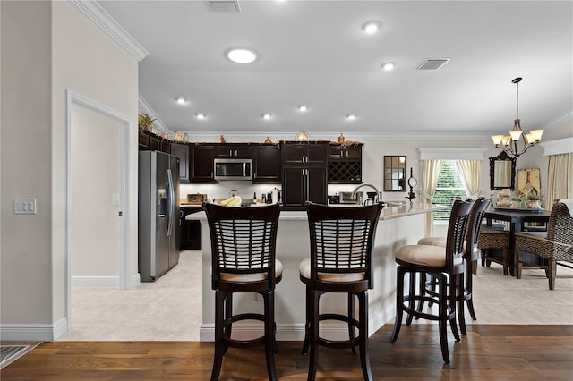 kitchen with light wood-type flooring, hanging light fixtures, ornamental molding, stainless steel appliances, and dark brown cabinets