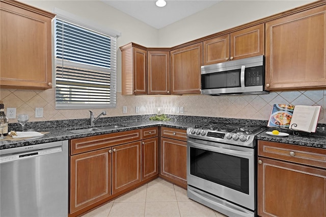 kitchen with sink, dark stone countertops, appliances with stainless steel finishes, tasteful backsplash, and light tile patterned flooring