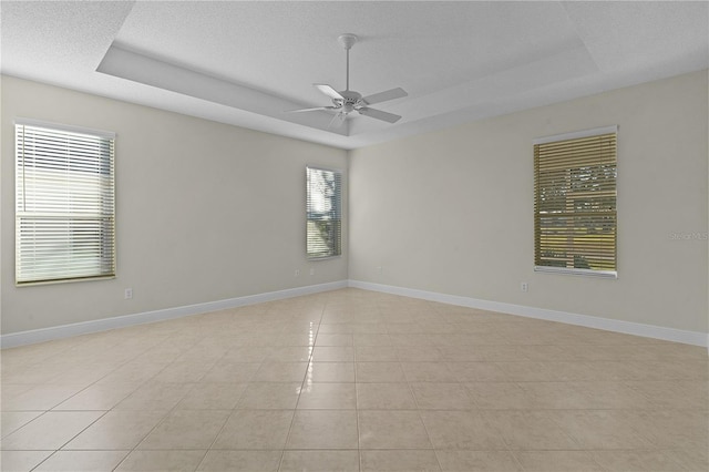 tiled spare room featuring ceiling fan and a tray ceiling