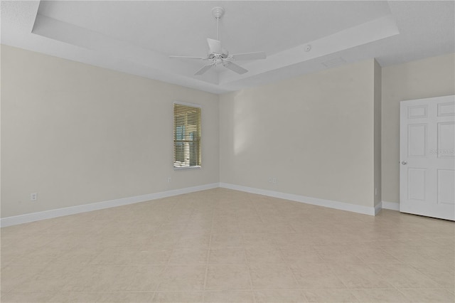 empty room with ceiling fan, a raised ceiling, and light tile patterned floors