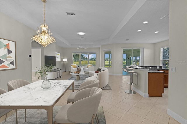 dining room with ceiling fan with notable chandelier, a raised ceiling, and light tile patterned flooring