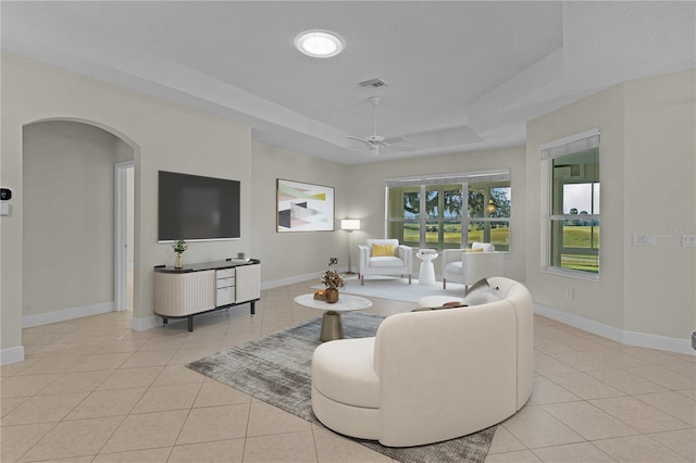 living room with ceiling fan, light tile patterned floors, and a tray ceiling