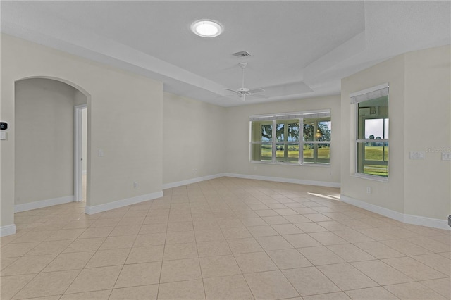 empty room with ceiling fan, light tile patterned flooring, and a raised ceiling