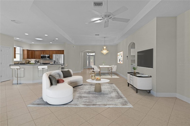 tiled living room with built in shelves, a raised ceiling, and ceiling fan