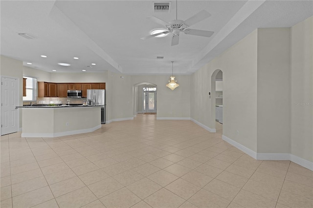 unfurnished living room with ceiling fan, light tile patterned flooring, and a tray ceiling