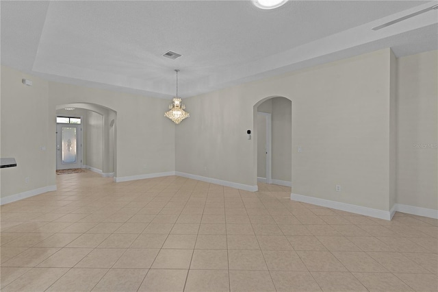 spare room with a raised ceiling, light tile patterned floors, and a textured ceiling