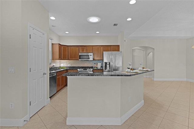 kitchen with decorative backsplash, dark stone counters, stainless steel appliances, light tile patterned floors, and a kitchen island