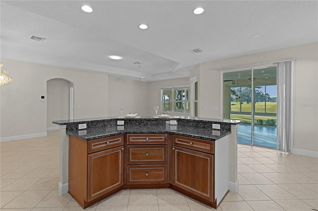 kitchen featuring a center island, light tile patterned floors, dark stone counters, and ceiling fan with notable chandelier