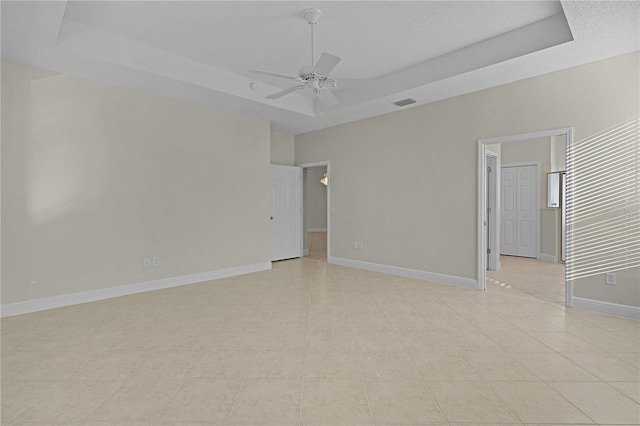 tiled spare room with a textured ceiling, a tray ceiling, and ceiling fan