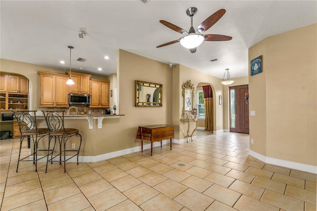 kitchen with light tile patterned flooring, stone countertops, a kitchen breakfast bar, kitchen peninsula, and decorative backsplash