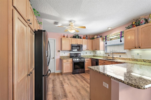 kitchen featuring stone counters, stainless steel appliances, visible vents, a sink, and a peninsula