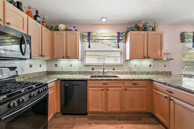 kitchen featuring stone countertops, wood finished floors, a healthy amount of sunlight, black appliances, and a sink