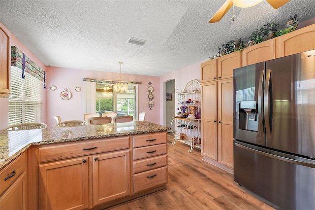 kitchen with visible vents, light wood-type flooring, stainless steel refrigerator with ice dispenser, light stone countertops, and pendant lighting