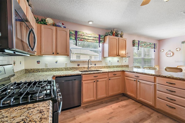 kitchen featuring light wood-style flooring, a sink, appliances with stainless steel finishes, light stone countertops, and tasteful backsplash