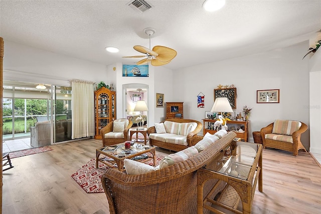 living area featuring a ceiling fan, light wood-type flooring, visible vents, and a textured ceiling