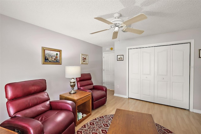 living area with light wood-type flooring, ceiling fan, a textured ceiling, and baseboards