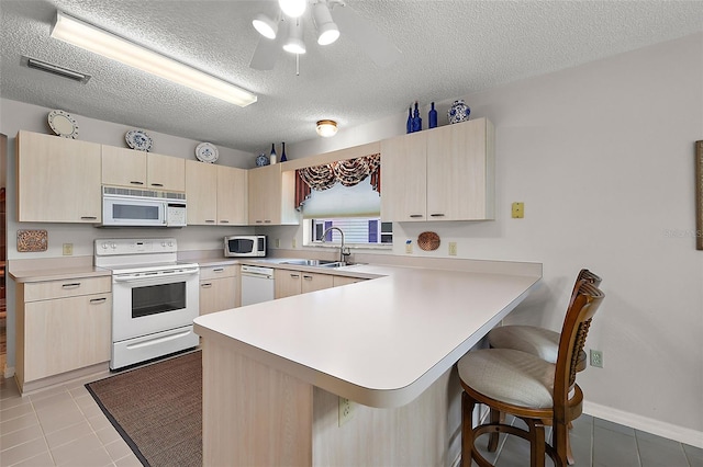 kitchen with sink, white appliances, a textured ceiling, light tile patterned floors, and kitchen peninsula