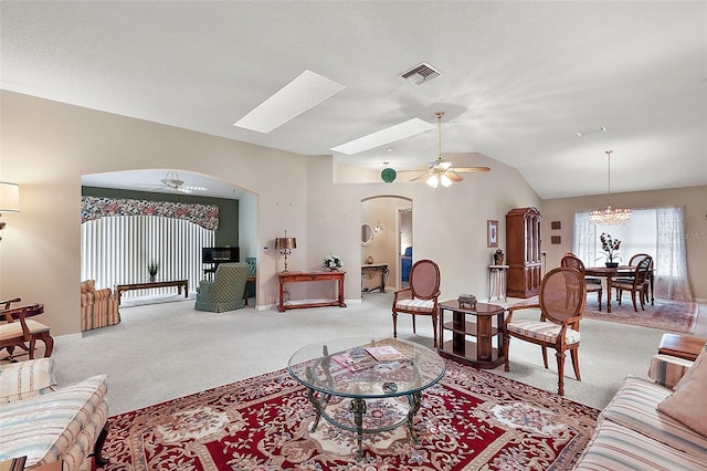 carpeted living room with vaulted ceiling with skylight and ceiling fan with notable chandelier