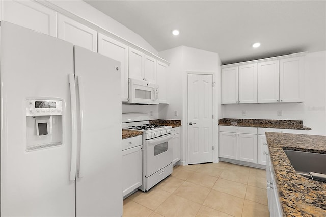 kitchen with white cabinets, dark stone counters, light tile patterned flooring, and white appliances