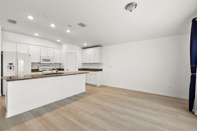 kitchen featuring light hardwood / wood-style flooring, white cabinetry, an island with sink, white appliances, and dark stone countertops