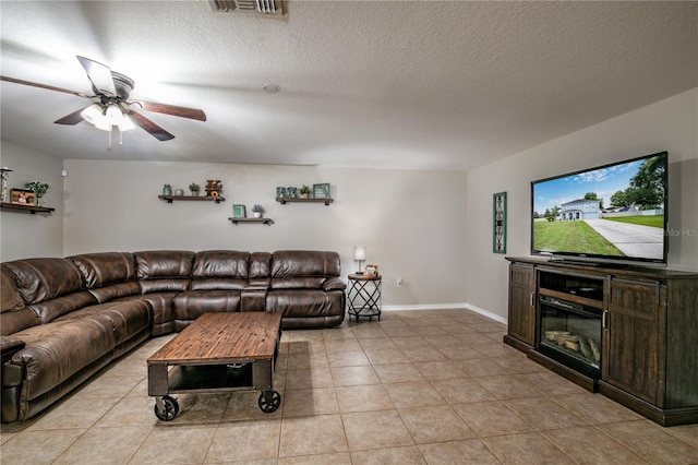 living area featuring light tile patterned floors, a textured ceiling, a ceiling fan, visible vents, and baseboards