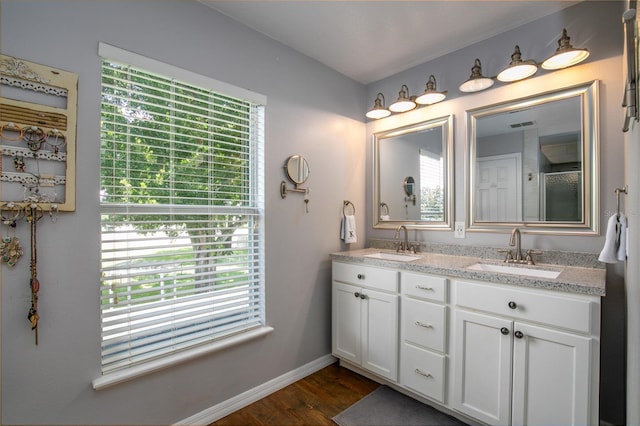 full bathroom with double vanity, wood finished floors, a sink, and baseboards