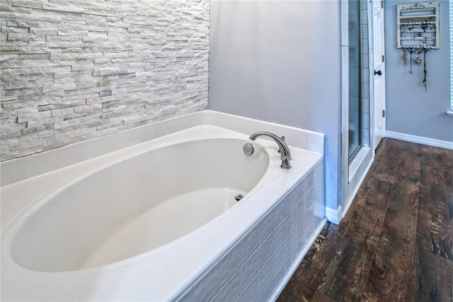 full bath with a shower stall, baseboards, a bath, and wood finished floors