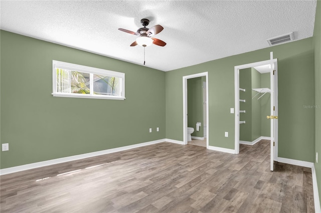 unfurnished bedroom featuring a textured ceiling, ensuite bath, a spacious closet, ceiling fan, and hardwood / wood-style flooring