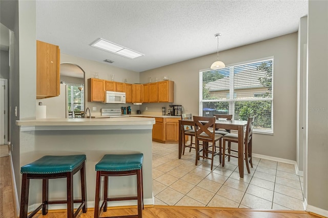 kitchen featuring stove, sink, hanging light fixtures, light tile patterned floors, and kitchen peninsula