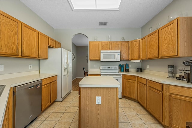 kitchen with a center island, white appliances, a textured ceiling, and light tile patterned floors