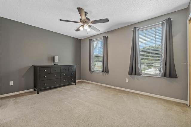 unfurnished bedroom featuring multiple windows, ceiling fan, light carpet, and a textured ceiling