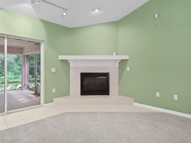 unfurnished living room with a tile fireplace, track lighting, and light colored carpet